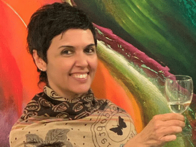 gallery.triums.ch - Künstlerin Ana Ramírez mit Glas in der Hand - ein Werk der Künstlerin im Hintergrund gallery.triums.ch - Künstlerin Ana Ramírez mit Glas in der Hand - ein Werk der Künstlerin im Hintergrund
